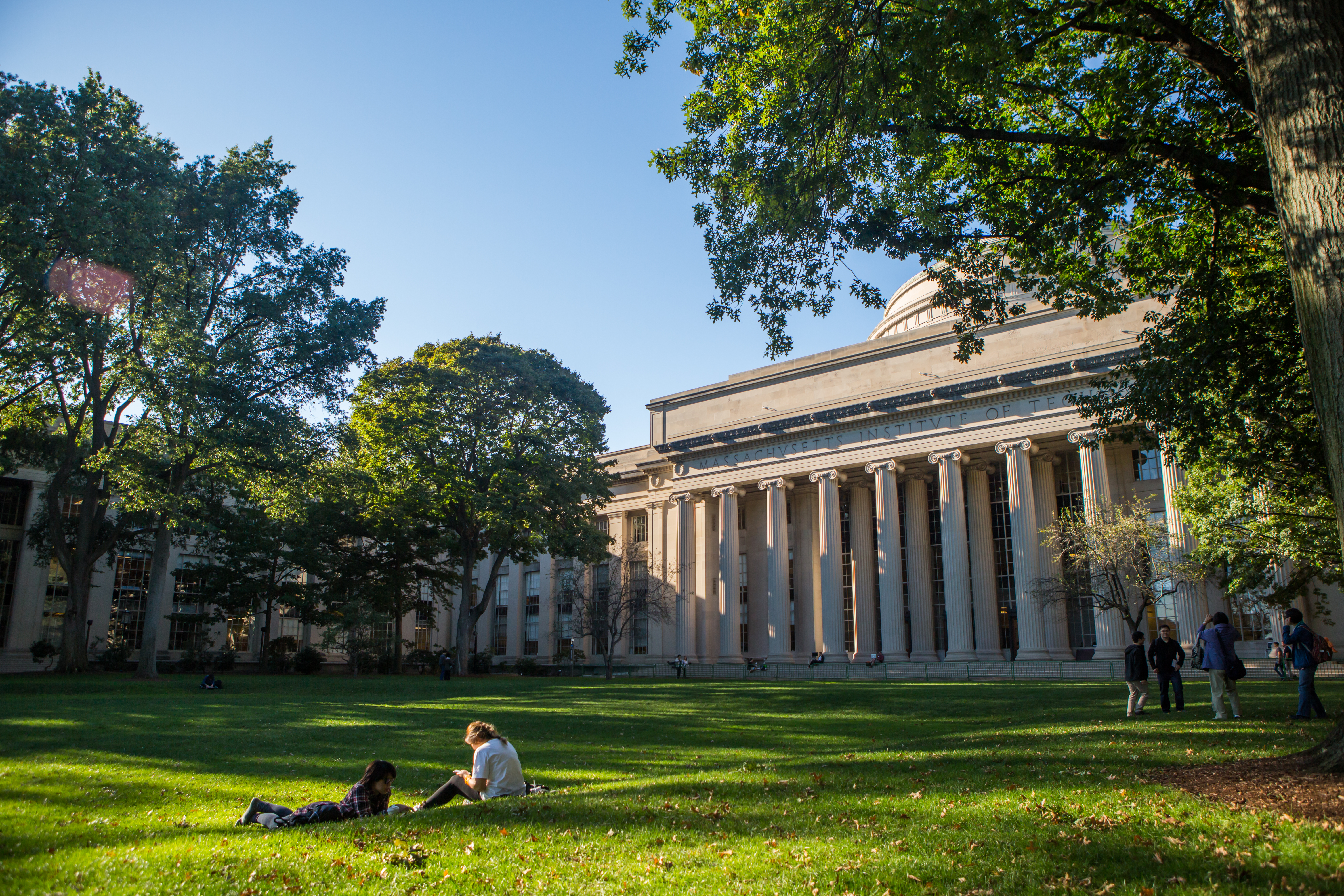 students lounge on a green lawn in front of the MIT dome