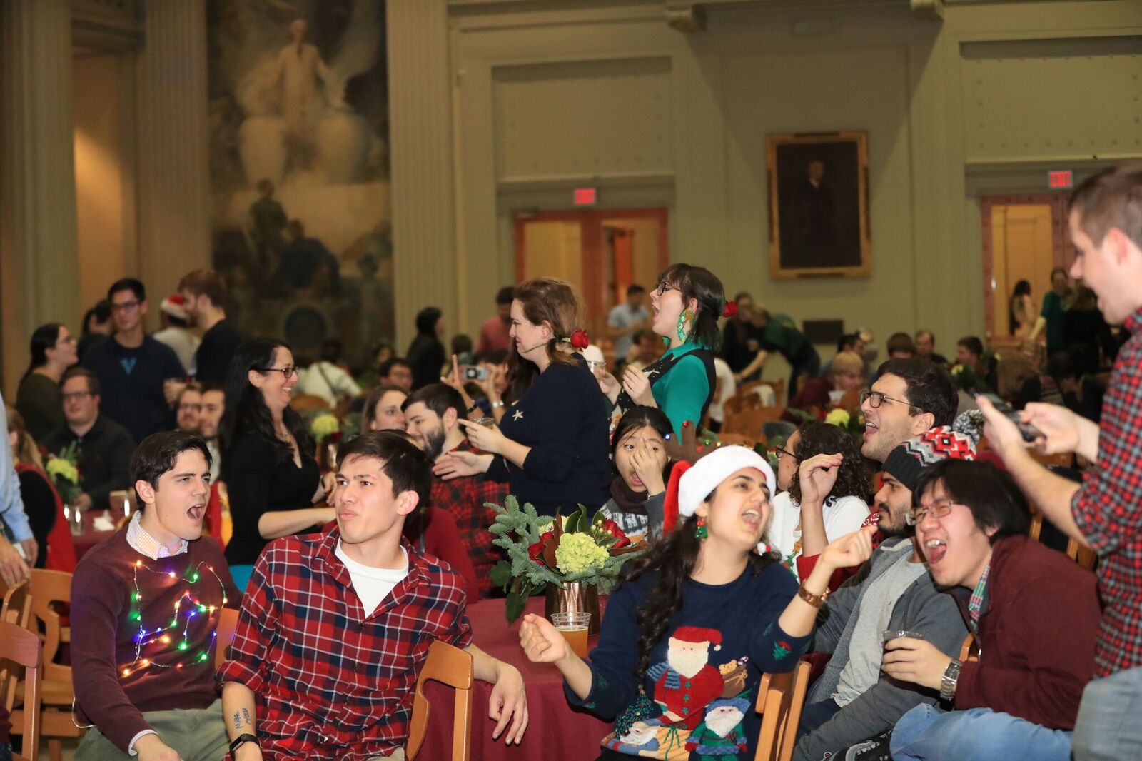 Members of the department of chemistry enjoy karaoke in a large ballroom while wearing festive holiday sweaters
