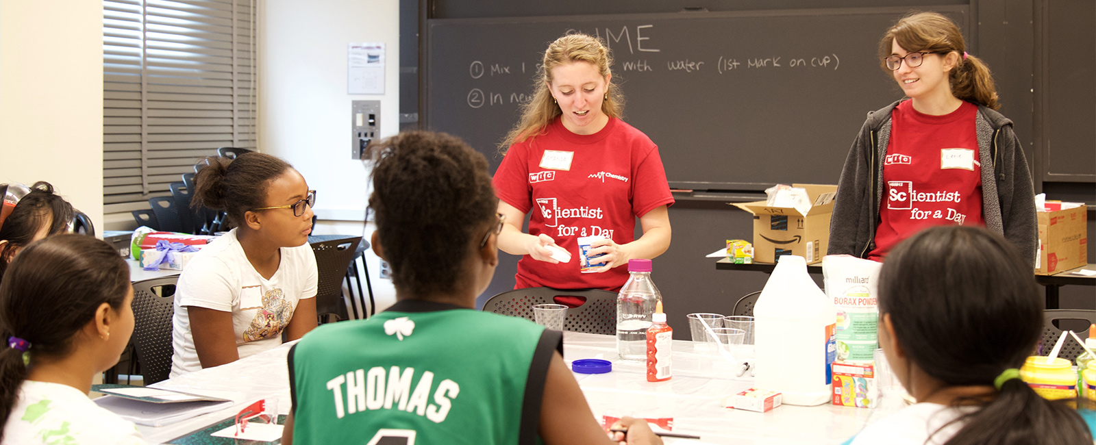 Two female graduate students lead a workshop of science demonstrations for middle school girls.