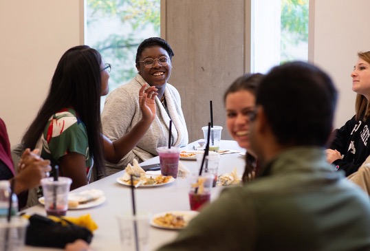 A group of young women engage in conversation around a breakfast table.