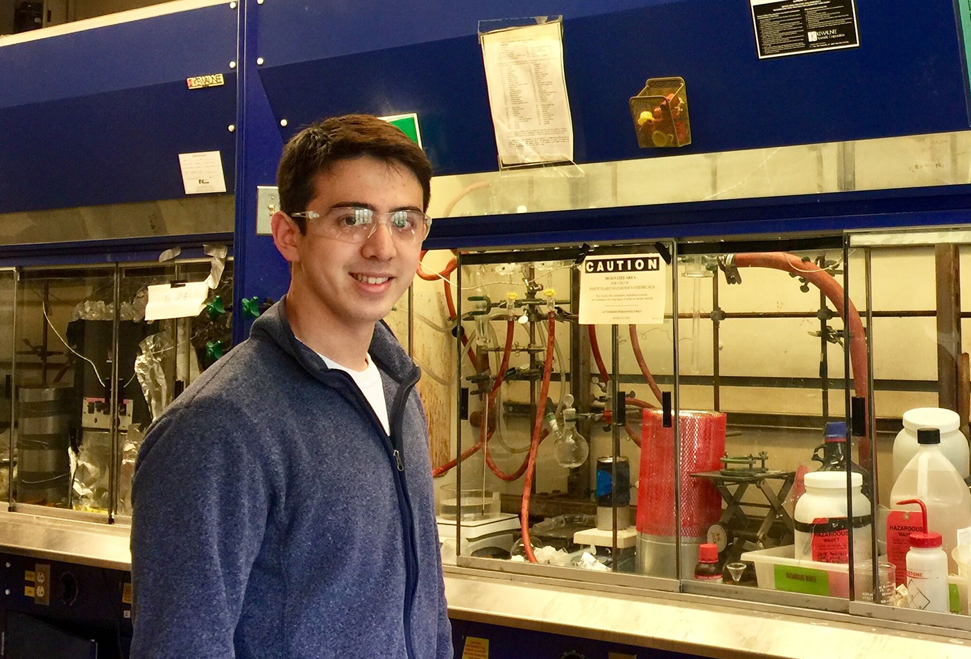 A male graduate student stands in front of a fume hood.