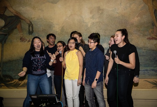 A large group of students perform karaoke on stage.
