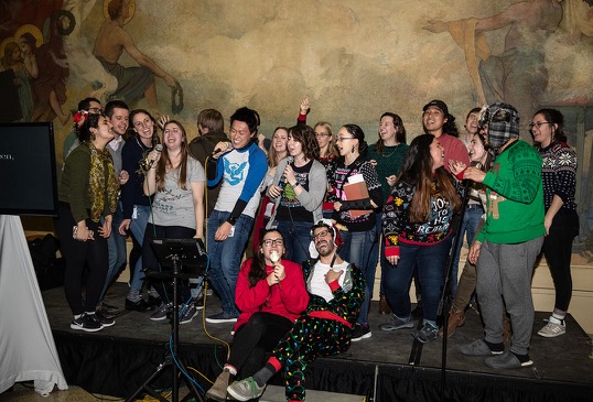 A large group of students perform karaoke on stage.