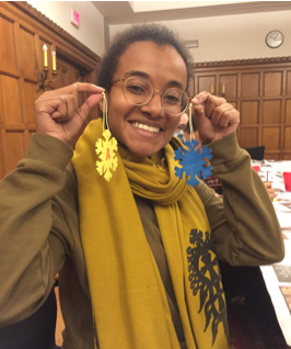 A woman wearing glasses holds up two handmade, bright yellow and blue, snowflake ornaments.