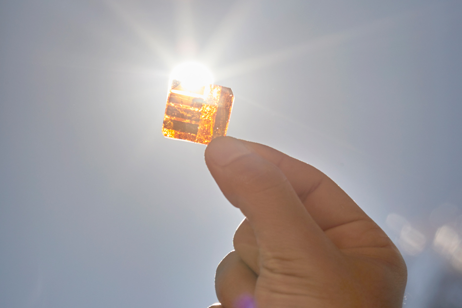 A hand holds a small, amber colored, square cell up to the sun.