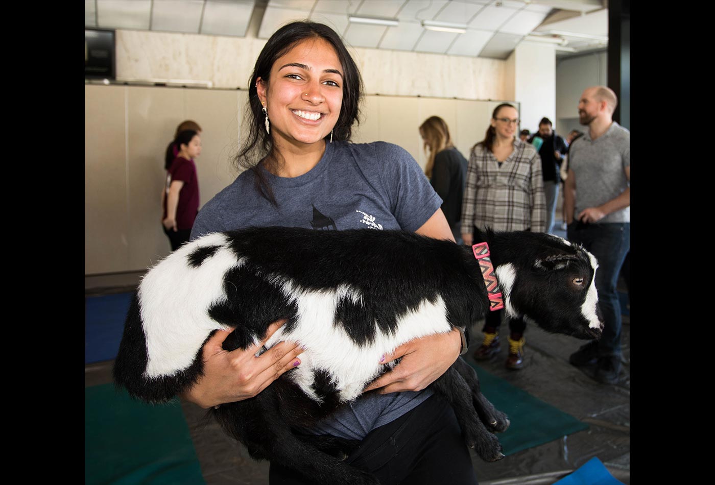 A female graduate student holds a black and white goat in her arms.