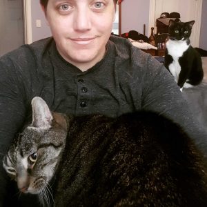 A person poses with two cats.