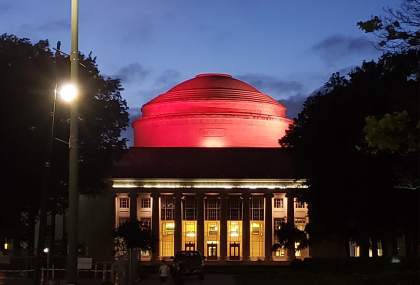 The MIT Dome lit up red at dusk.