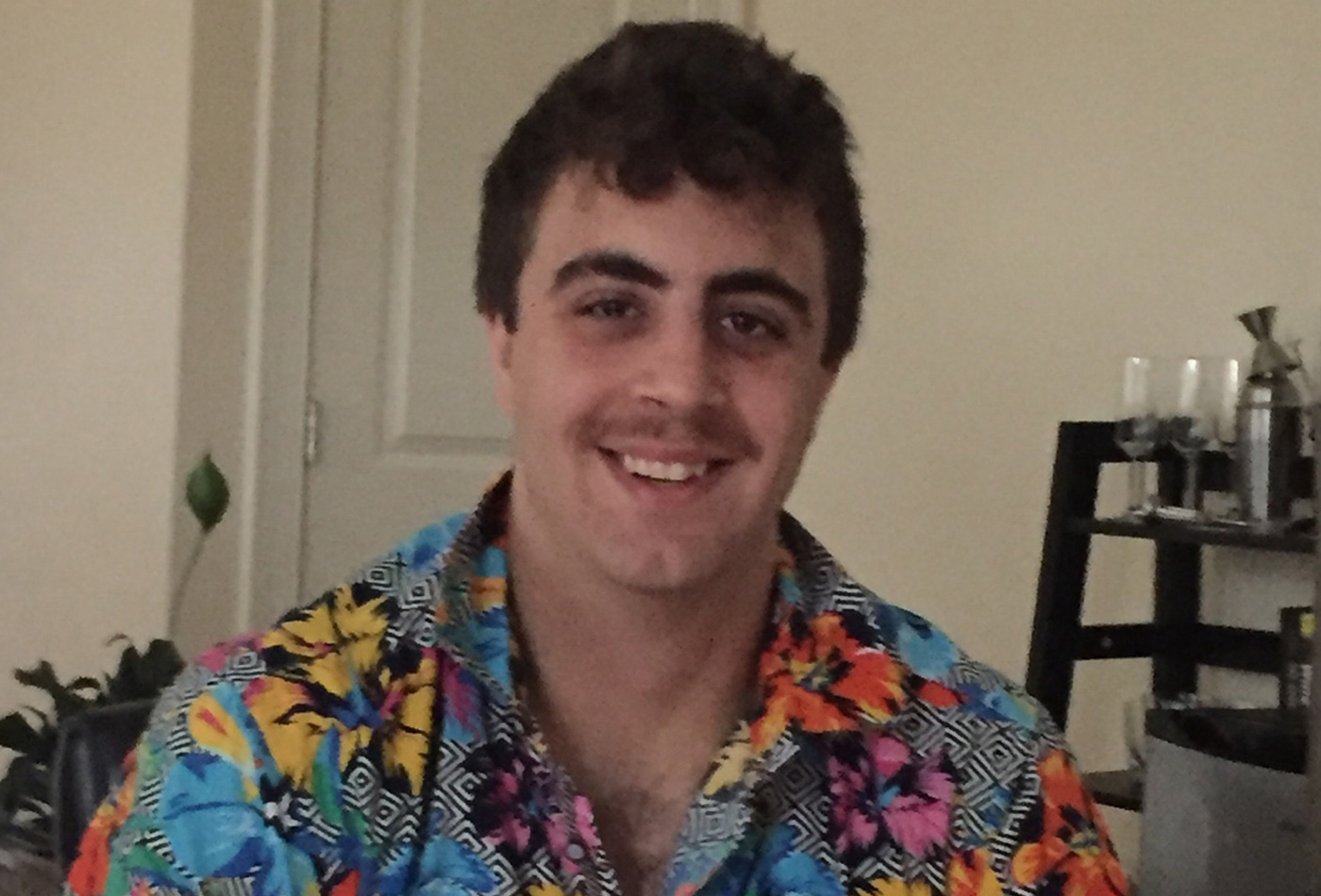 A male graduate student smiles while wearing a tropical shirt.
