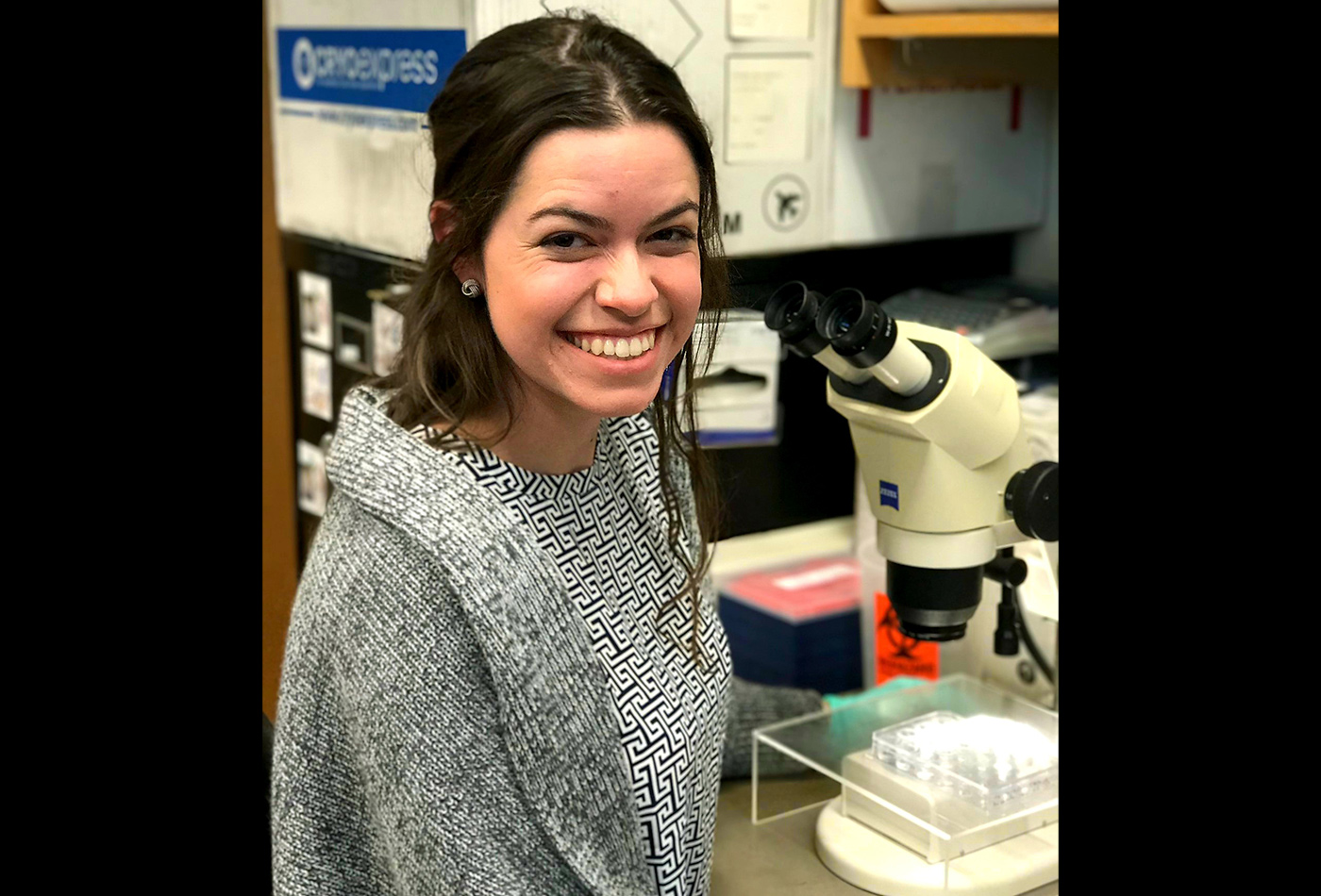 A female graduate student smiles while sitting at a microscope