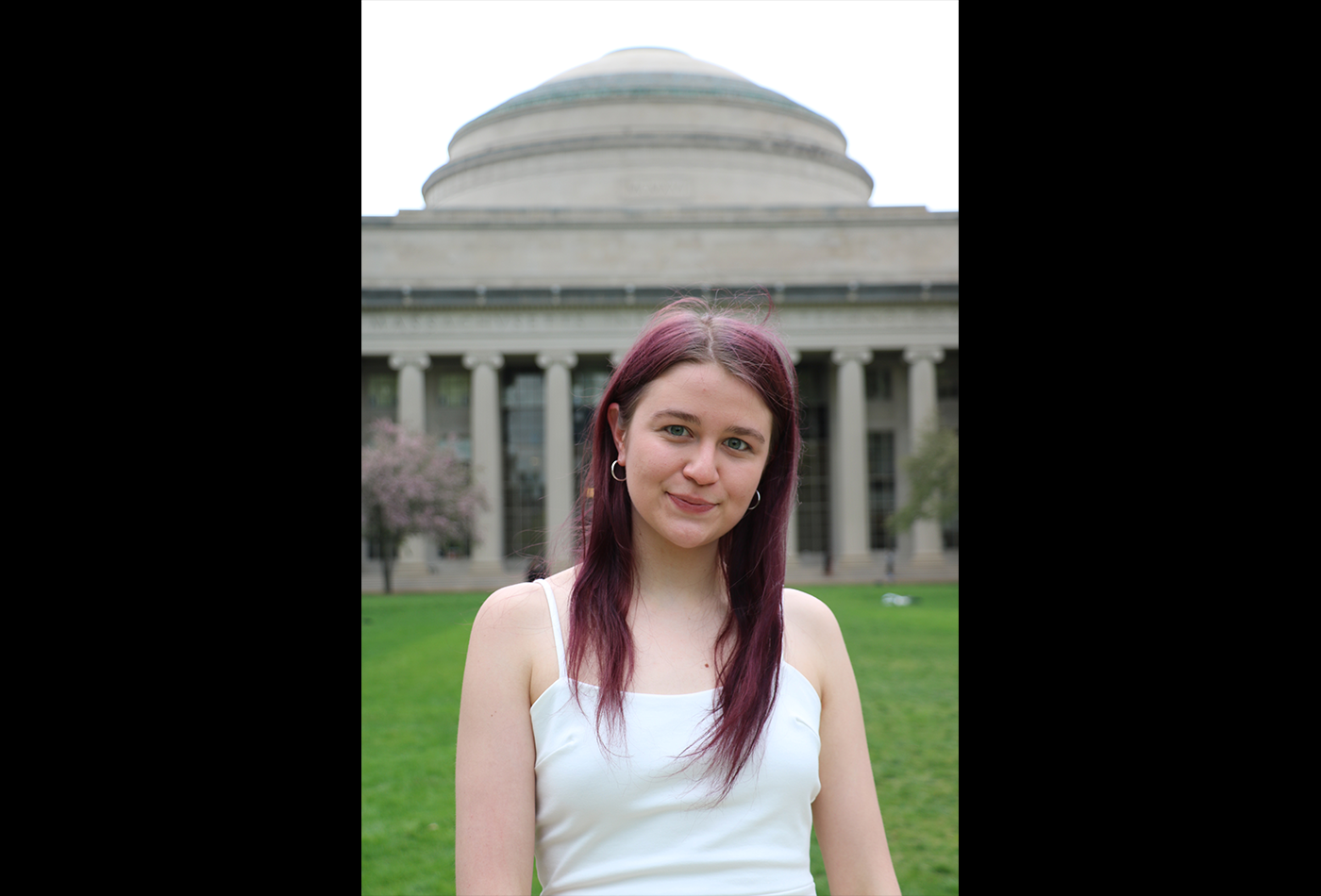 A young woman stands in front of the MIT Dome.