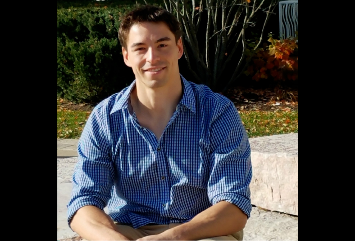 A male graduate student smiles outside.