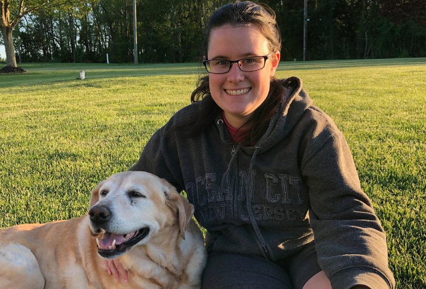 A woman smiles beside a yellow lab.