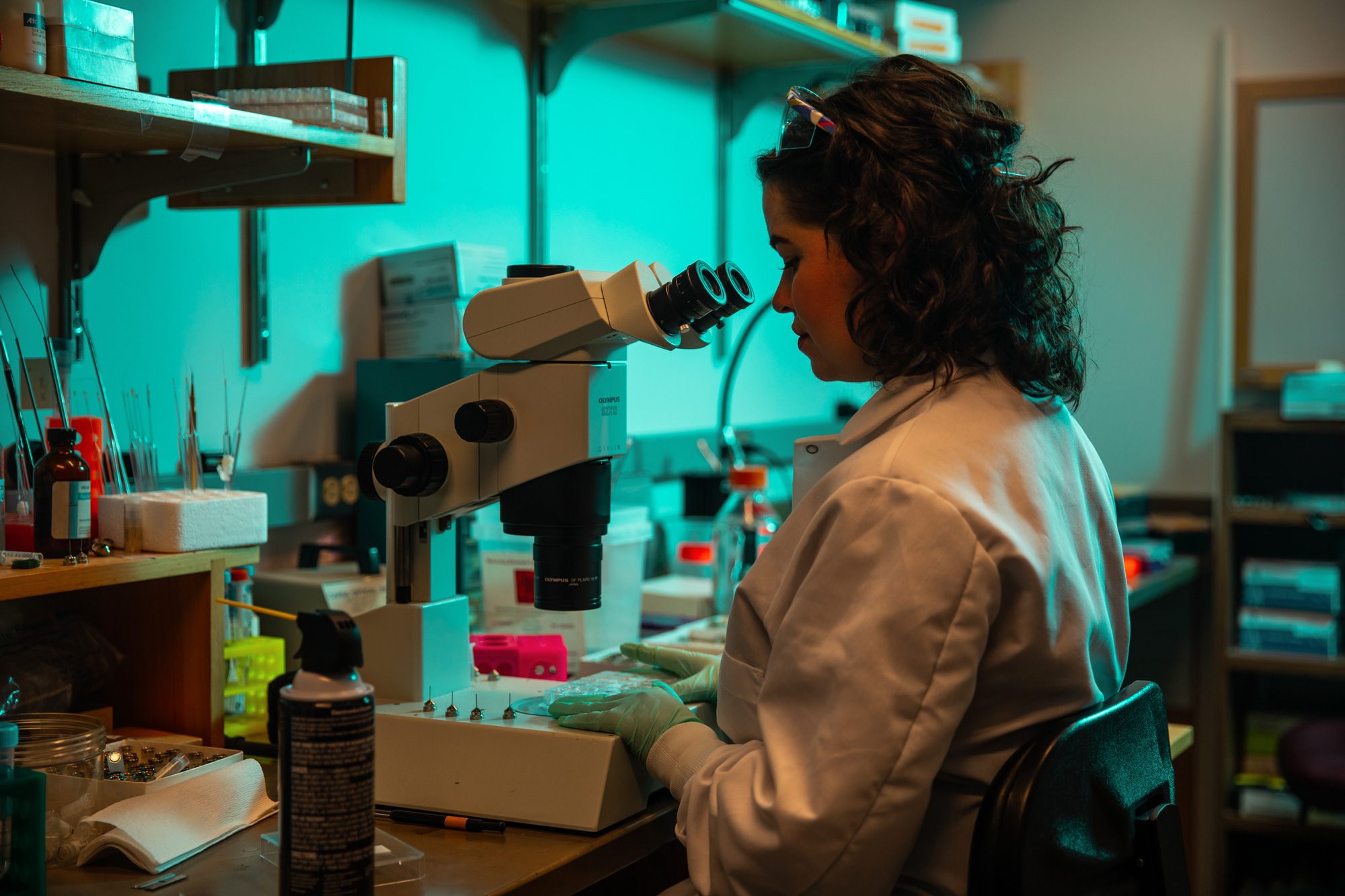A woman in a lab coat looks into a microscope.