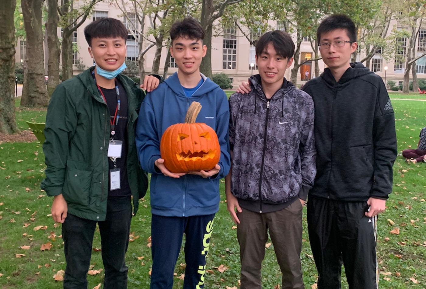 Four graduate students pose with a carved pumpkin.