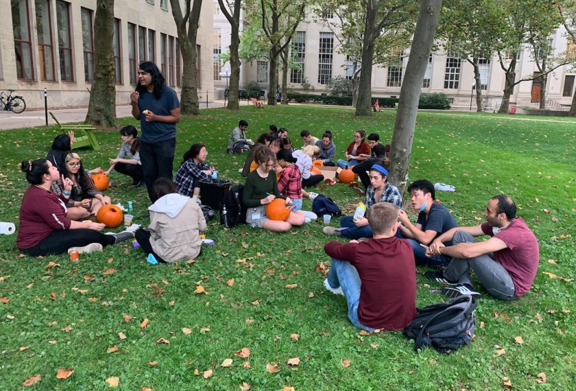 A group of students carve pumpkins on the grass.
