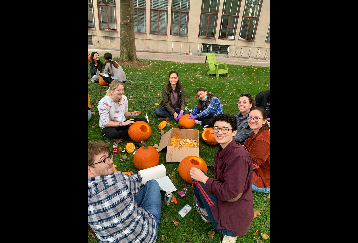 A group of students carve pumpkins on the grass.