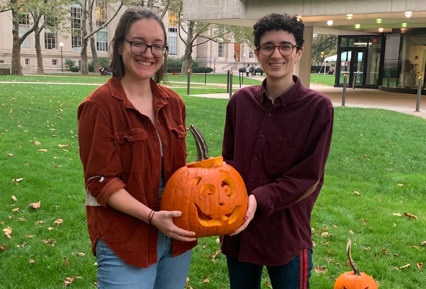 Two graduate students pose with their carved pumpkin