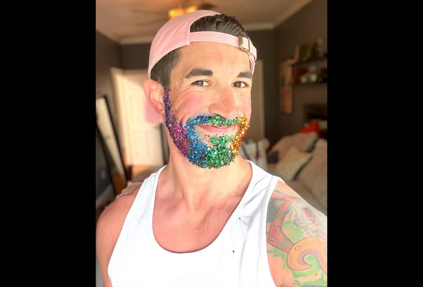 A man with a beard covered in rainbow glitter smiles.