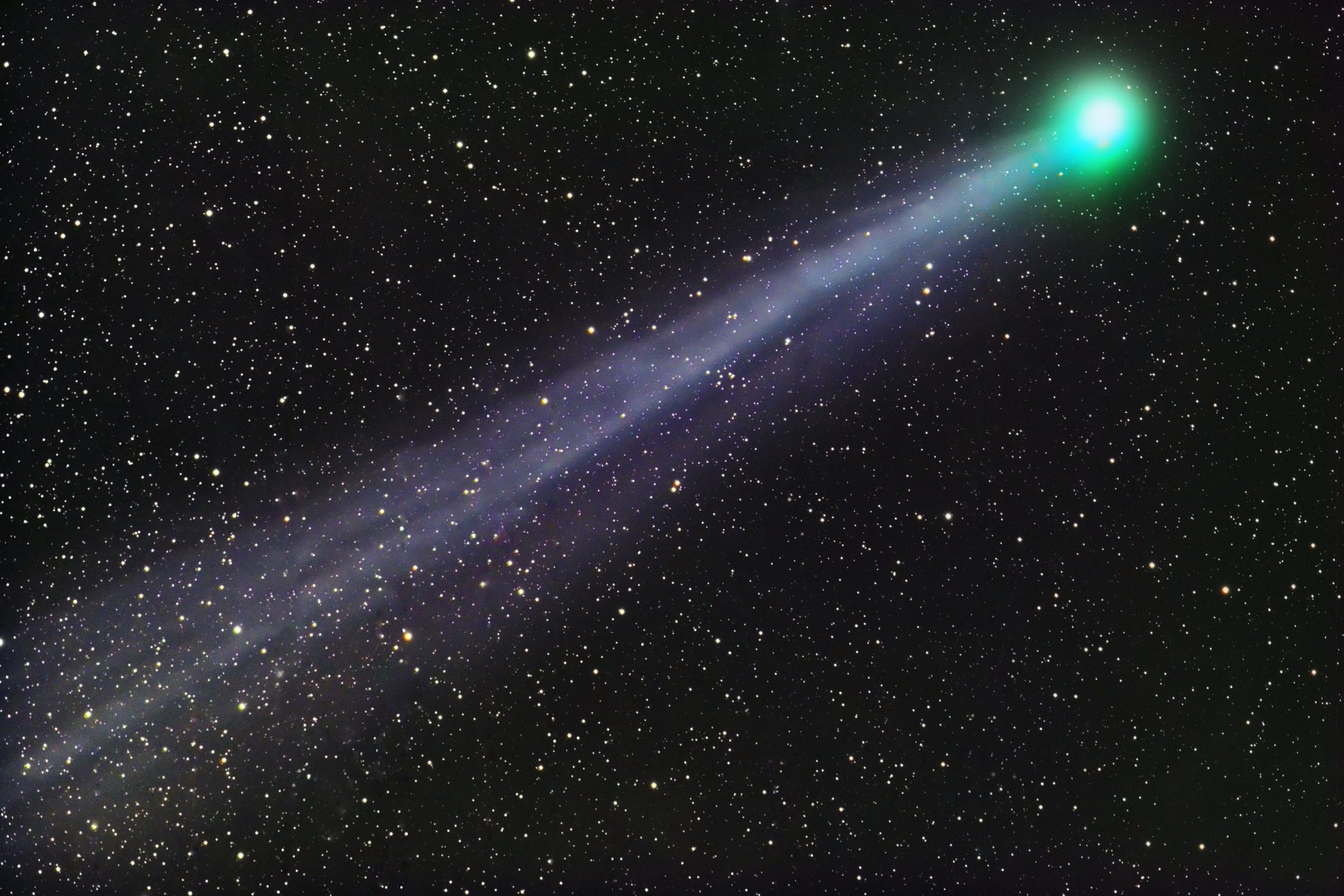 A comet streaks across a dark background, green head in the top right and tail stretching to bottom left.