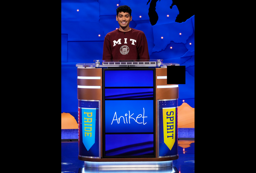 The subject in MIT logo sweatshirt stands behind a podium with the name Aniket