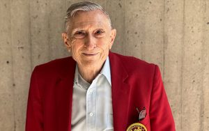 An older man in a red blazer smiles.