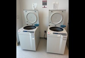 Two white centrifuges resembling top loading washing machines sit side by side in the lab.