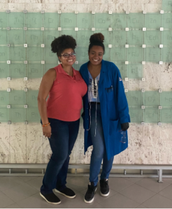 Michelle Gaines and Taylor Talley smile side by side in front of a glass periodic table sculpture.