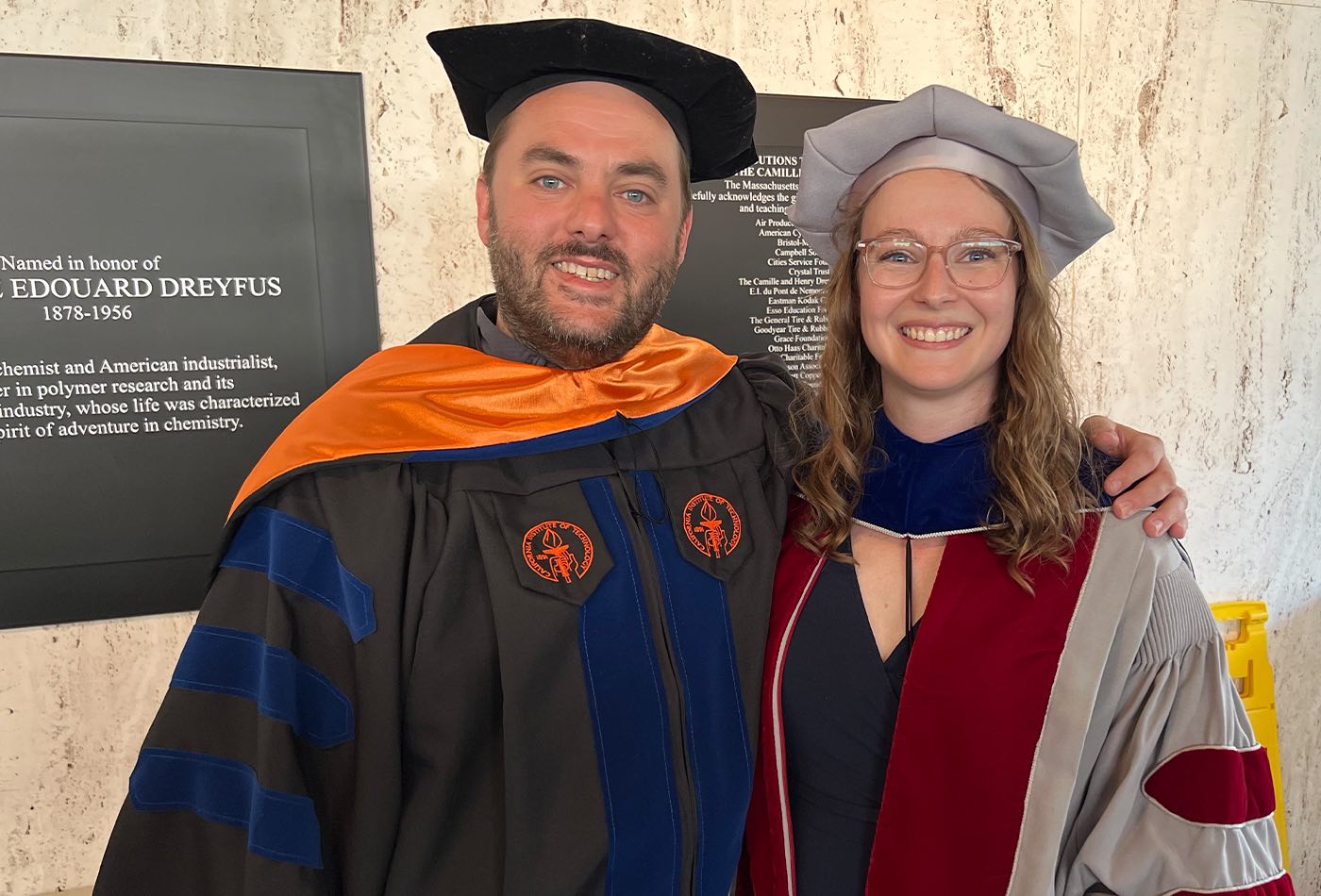 Professor Dan Suess smiles with his PhD student, Alexandra Brown, both in regalia.
