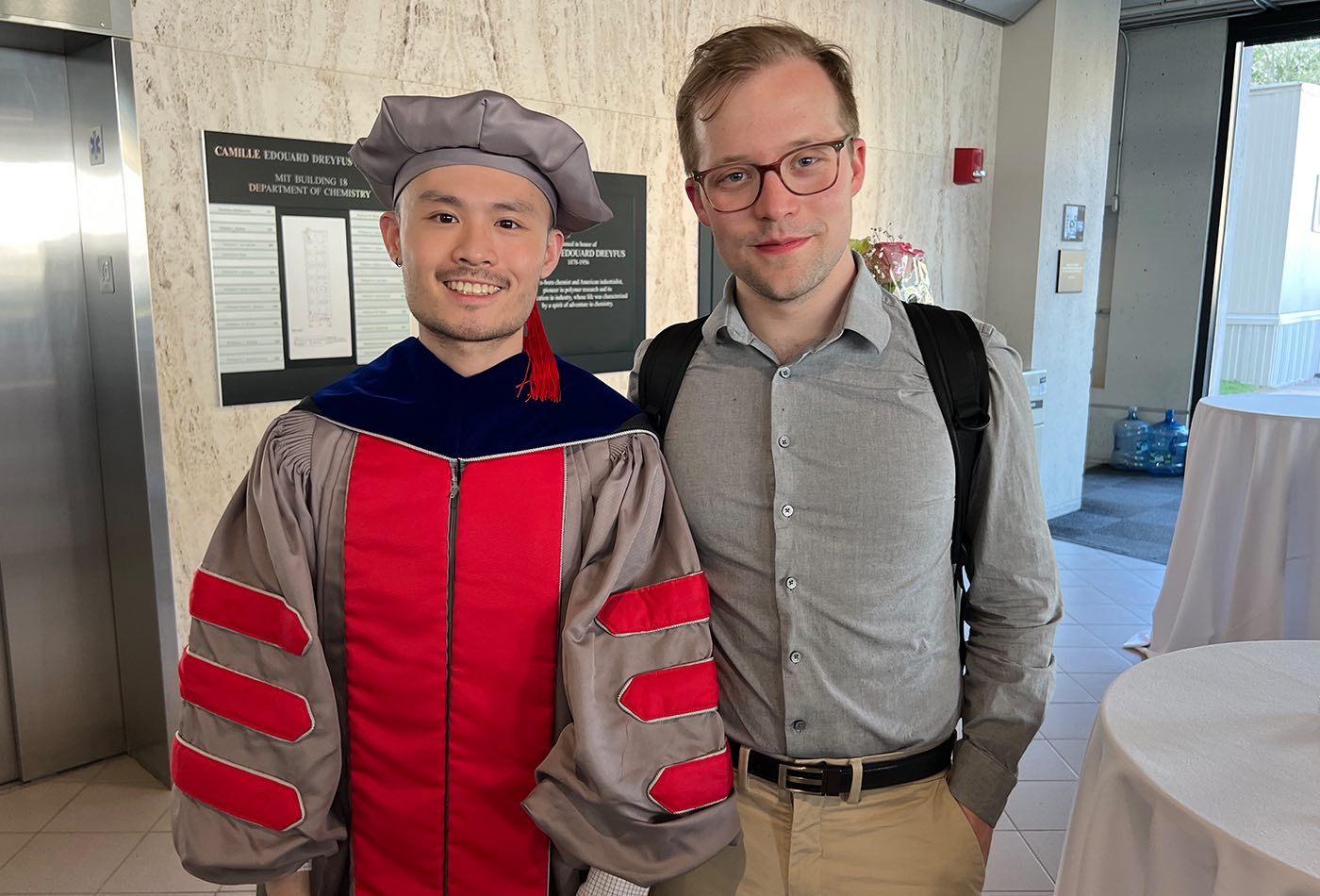 Juanye Zhang, wearing his hooding regalia, smiles beside a guest at the Advanced Degree Conferral ceremony.
