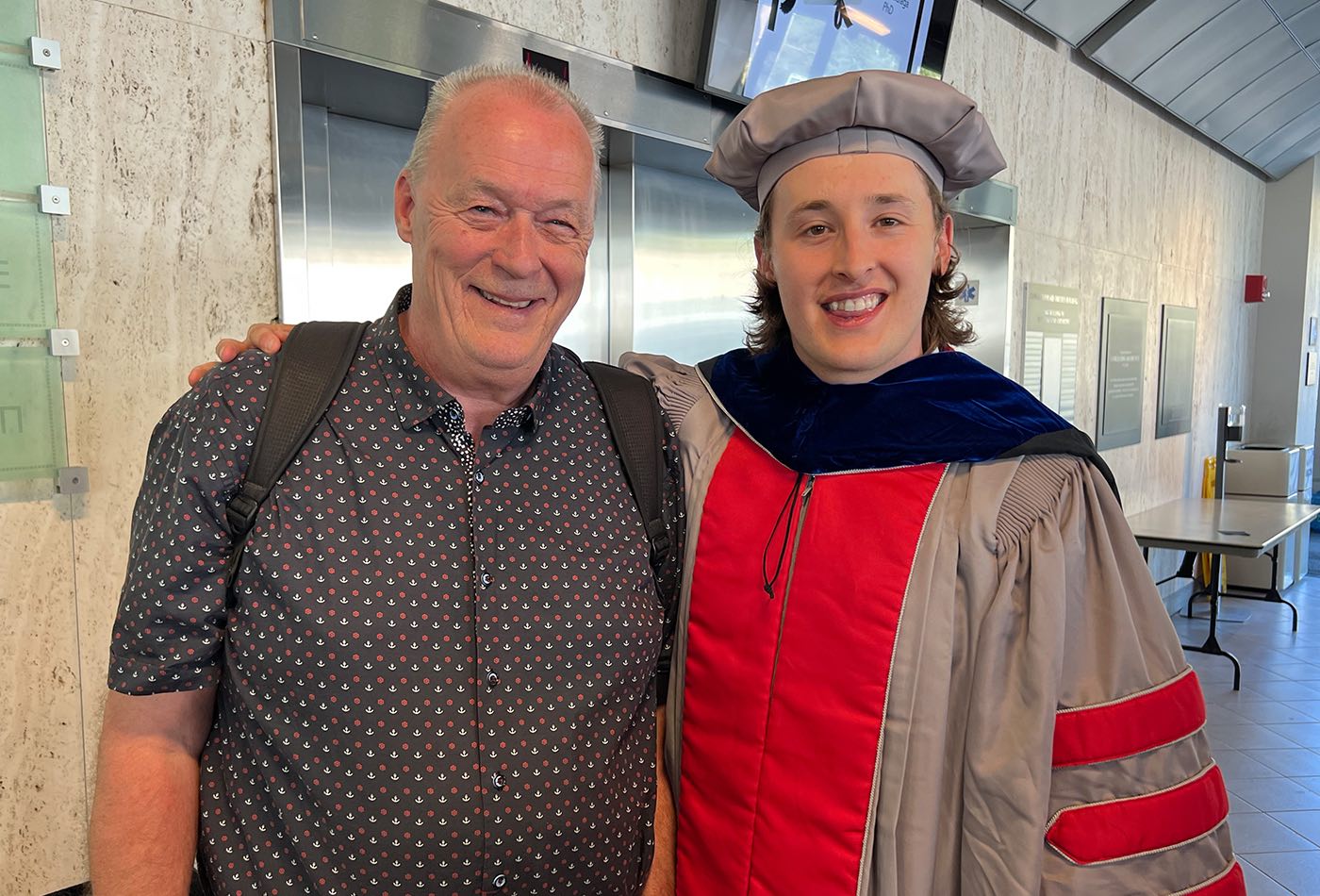 Leo Delage-Laurin, a PhD recipient, smiles in his regalia beside an older man, his guest.