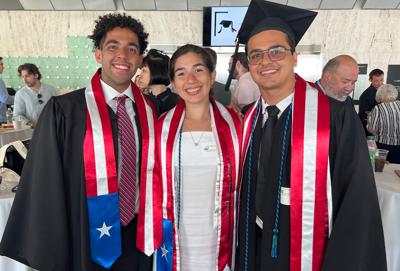Gabriel Caamaño, Gabriella Aponte, and Pedro Colon smile in their graduation robes at the reception event.