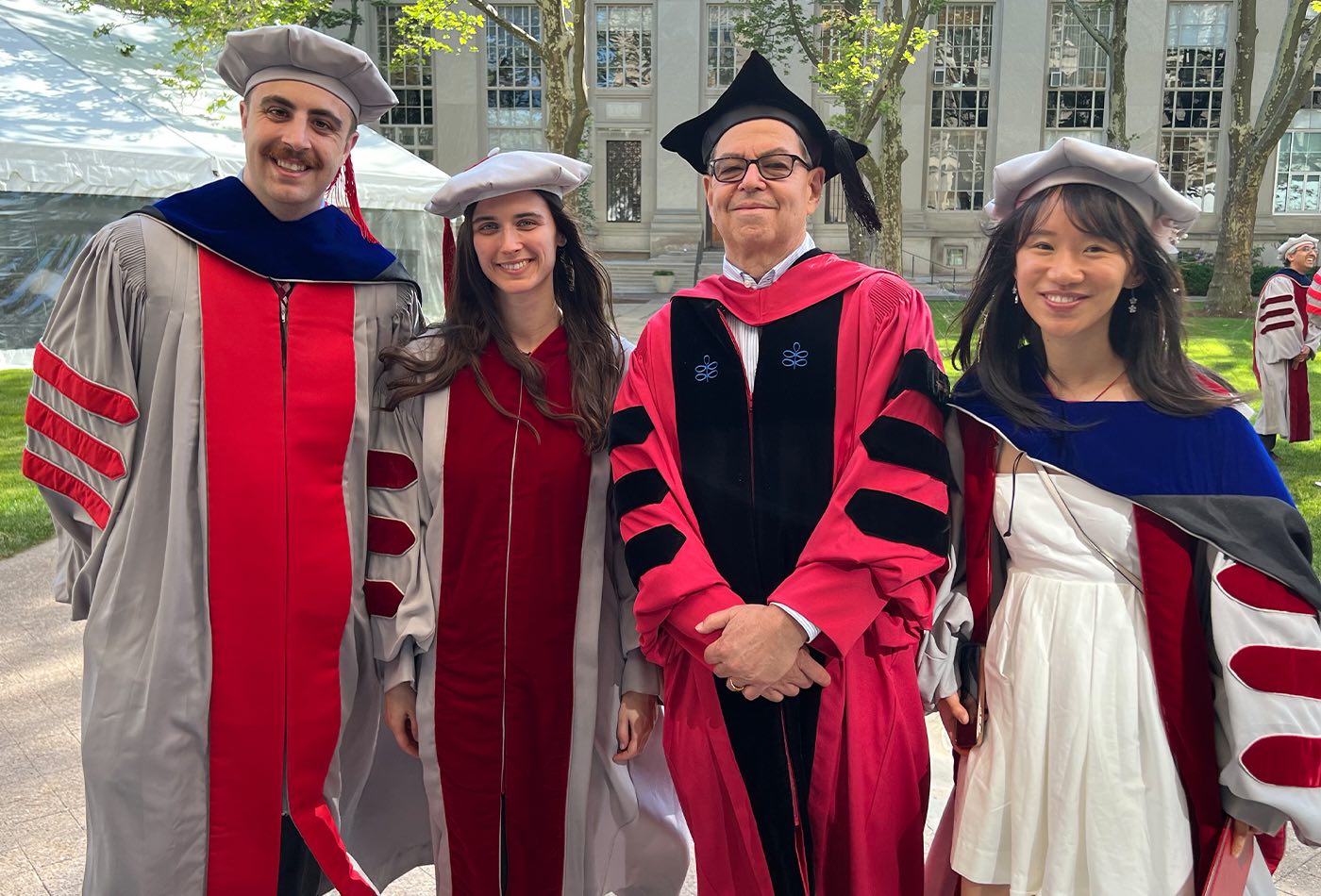 Professor Steve Buchwald smiles with three newly minted PhD recipients from his research group, all in regalia.
