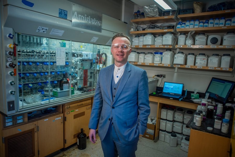 Brad Pentelute smiles in his lab, wearing a suit and eye protection.
