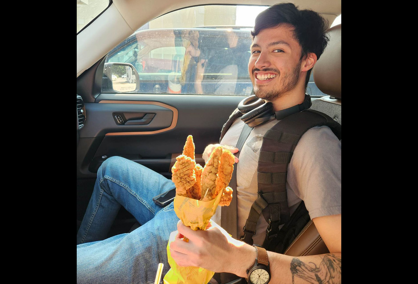 Roberto Herrera smiles in a car holding a bouquet of chicken tenders.