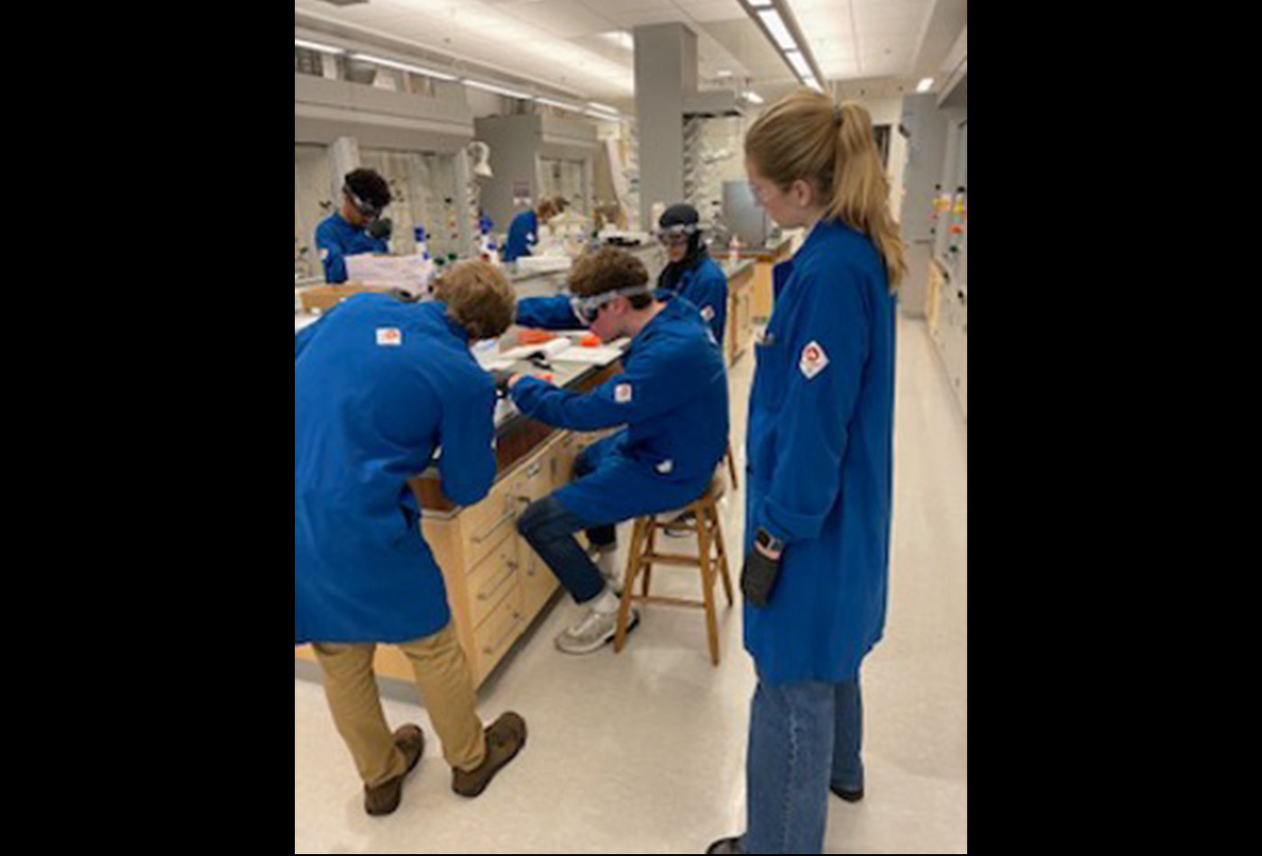 A group of students in lab coats mill about a lab.
