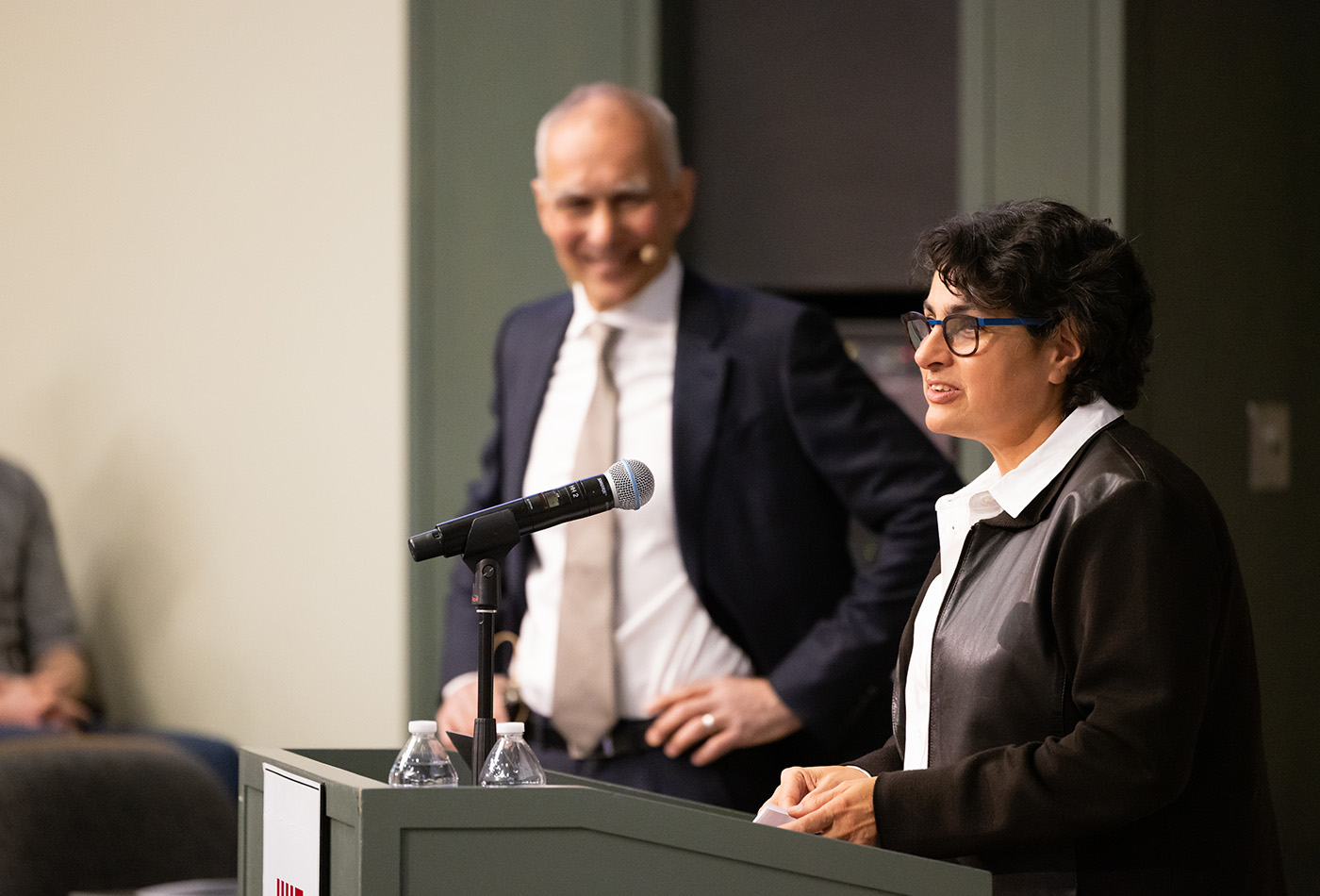 Dean Mavalvala stands at a podium with Moungi Bawendi in the background.