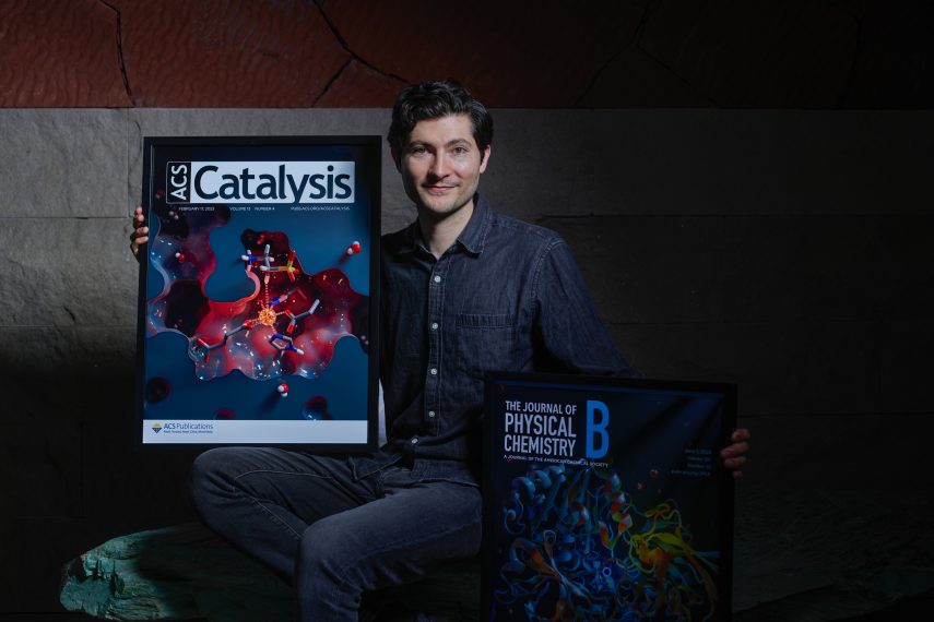 David Kastner holds two posters of journal covers showing his 3D art. The titles are “ACS Catalysis” and “Journal of Physical Chemistry.”