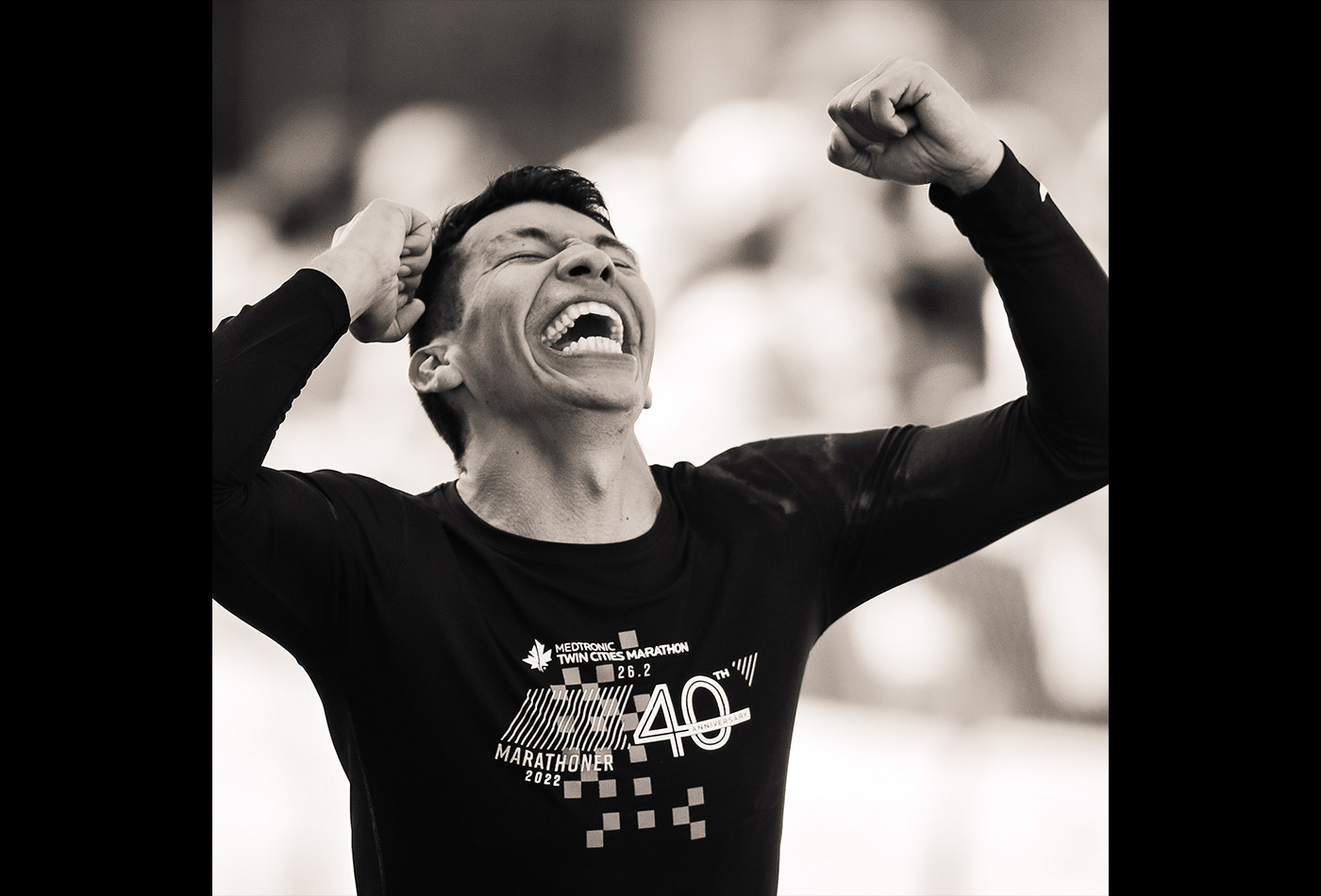 Juan Felipe celebrates as he crosses a marathon finish line in this black and white photo.