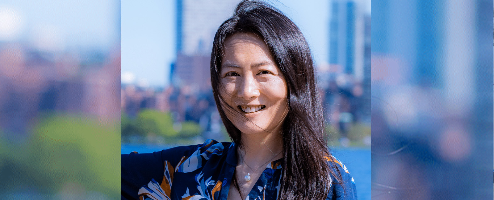 Yang Shao-Horn smiles outdoors with the Boston skyline behind her.