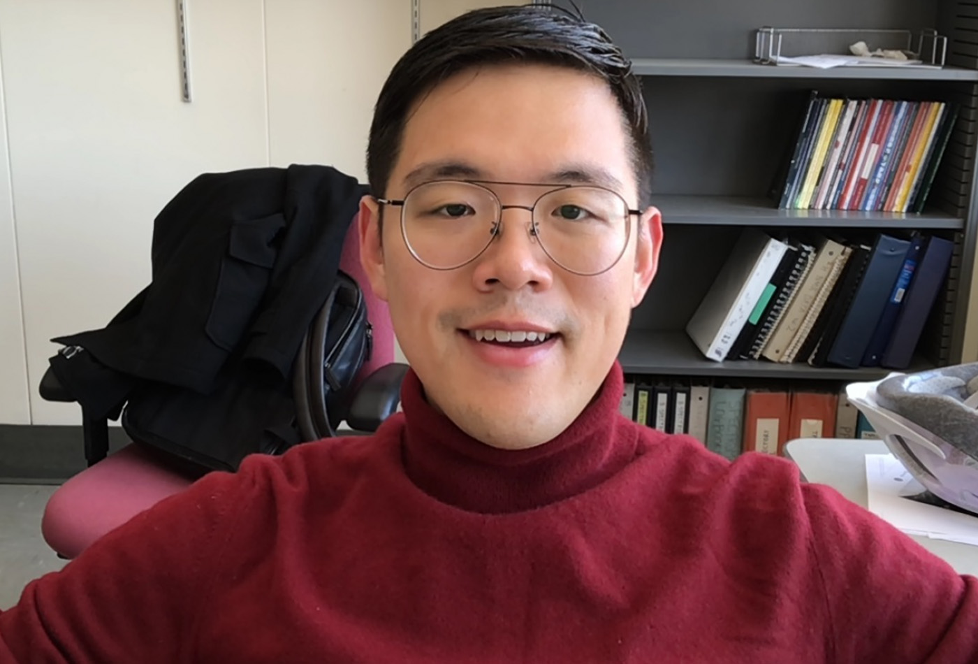 Yifan Quan smiles in his office wearing a red turtleneck.