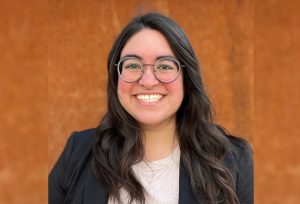 Whitney Hess smiles in front of a dark orange background.