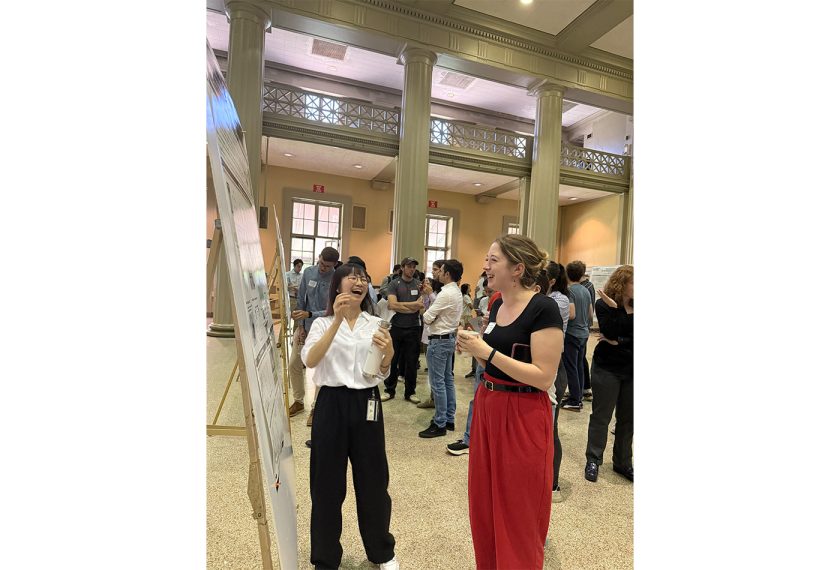 Chi Hsien-Wang and Molly Warndorf stand in front of a poster, reading its content.