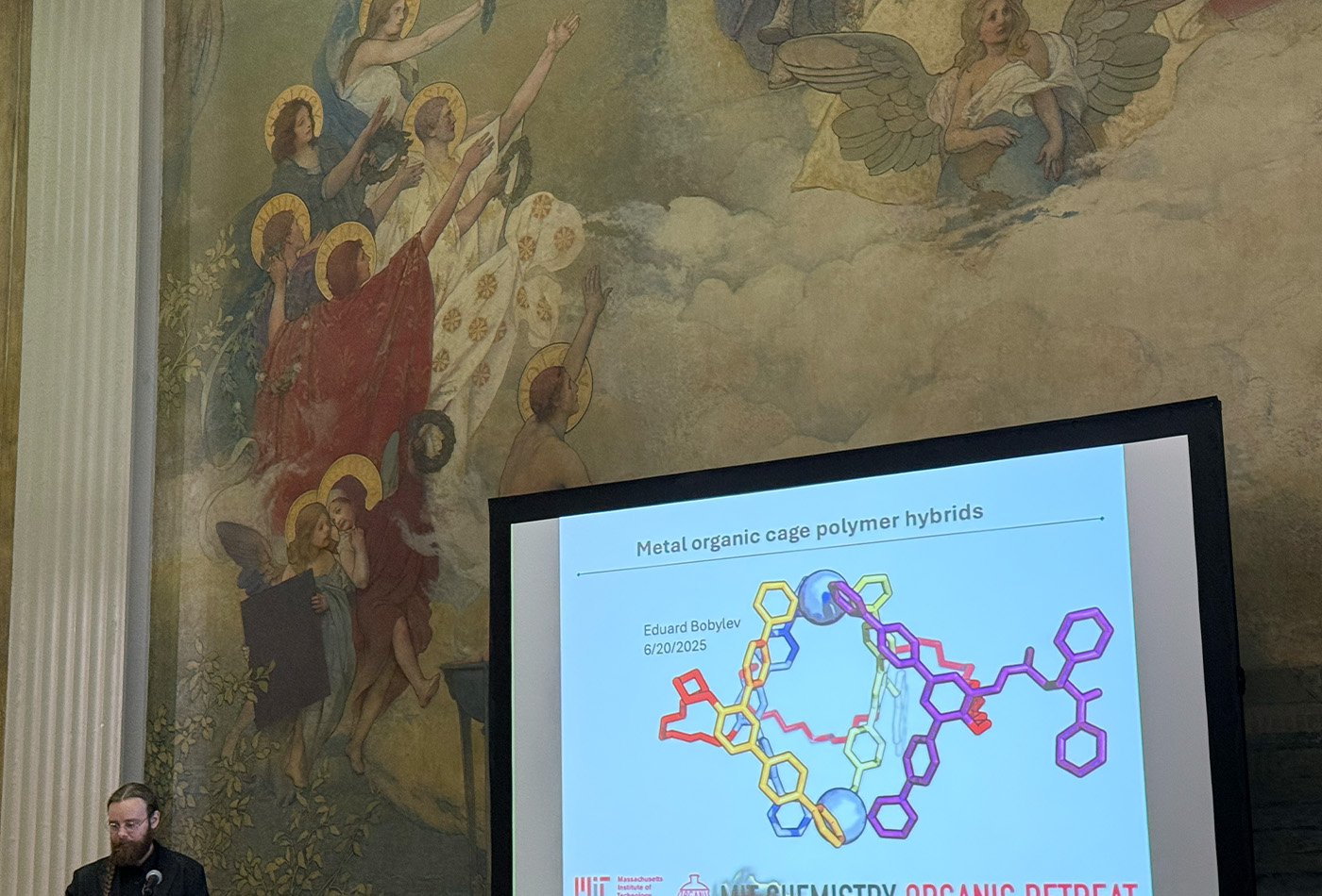 Eduard Bobylev stands in front of a wall and a projection screen.