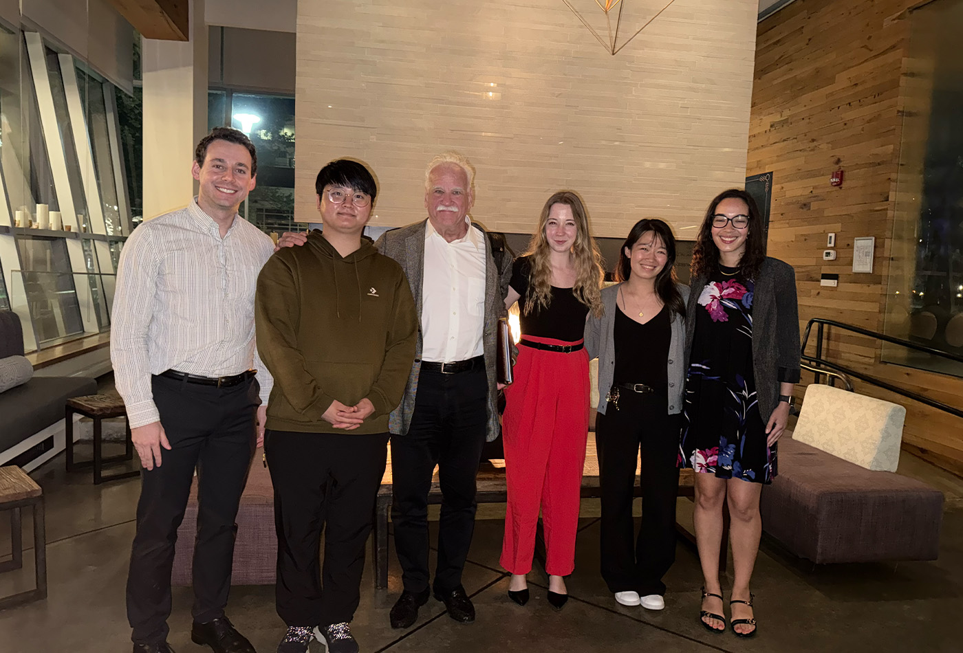 A row of students, postdocs, and faculty smile in front of a wall.