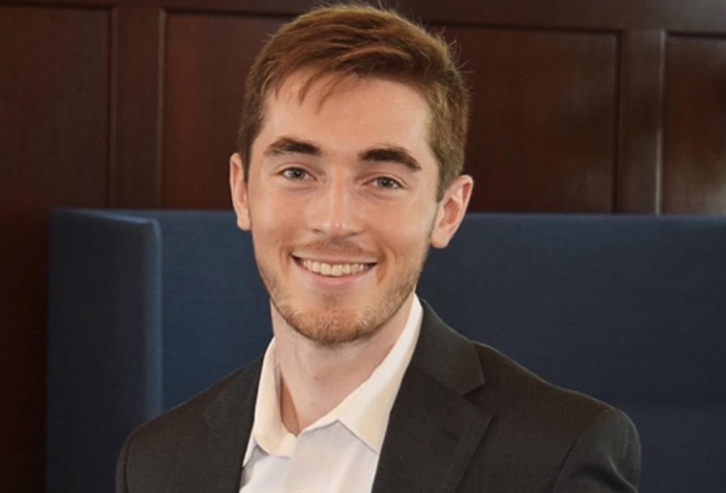 Nate Somers smiles in front of a dark background.