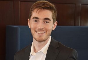 Nate Somers smiles in front of a dark background.