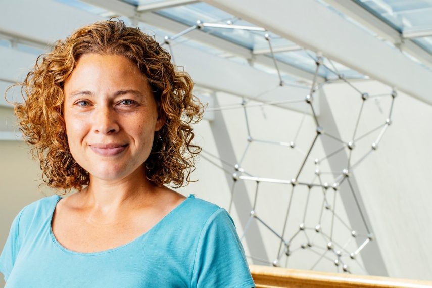 Professor Danna Freedman smiles in front of a silver sculpture.