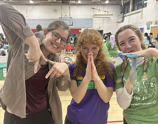 Three women spell out MIT with their hands.