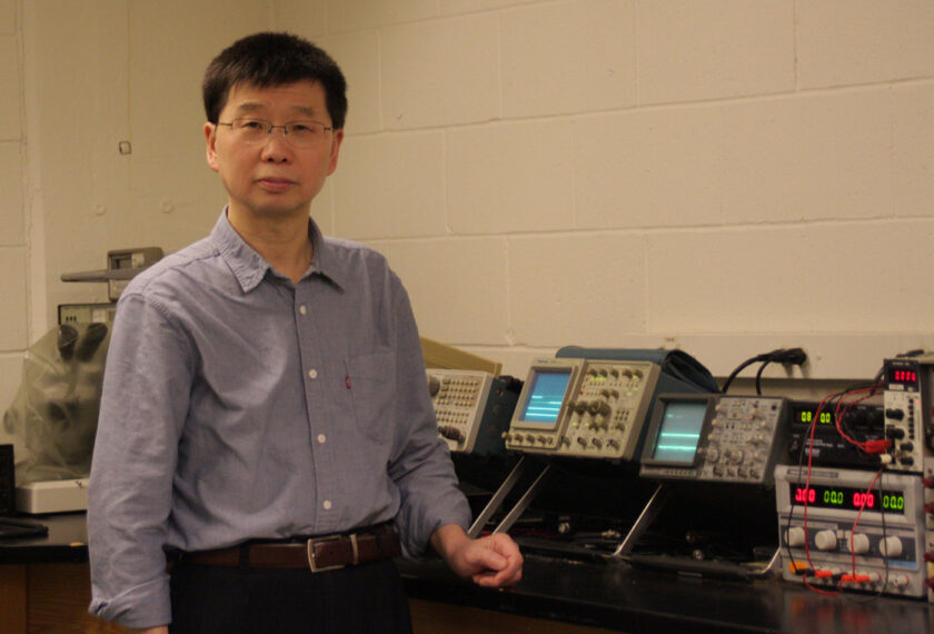 Gang Liu smiles in his office among many machines.
